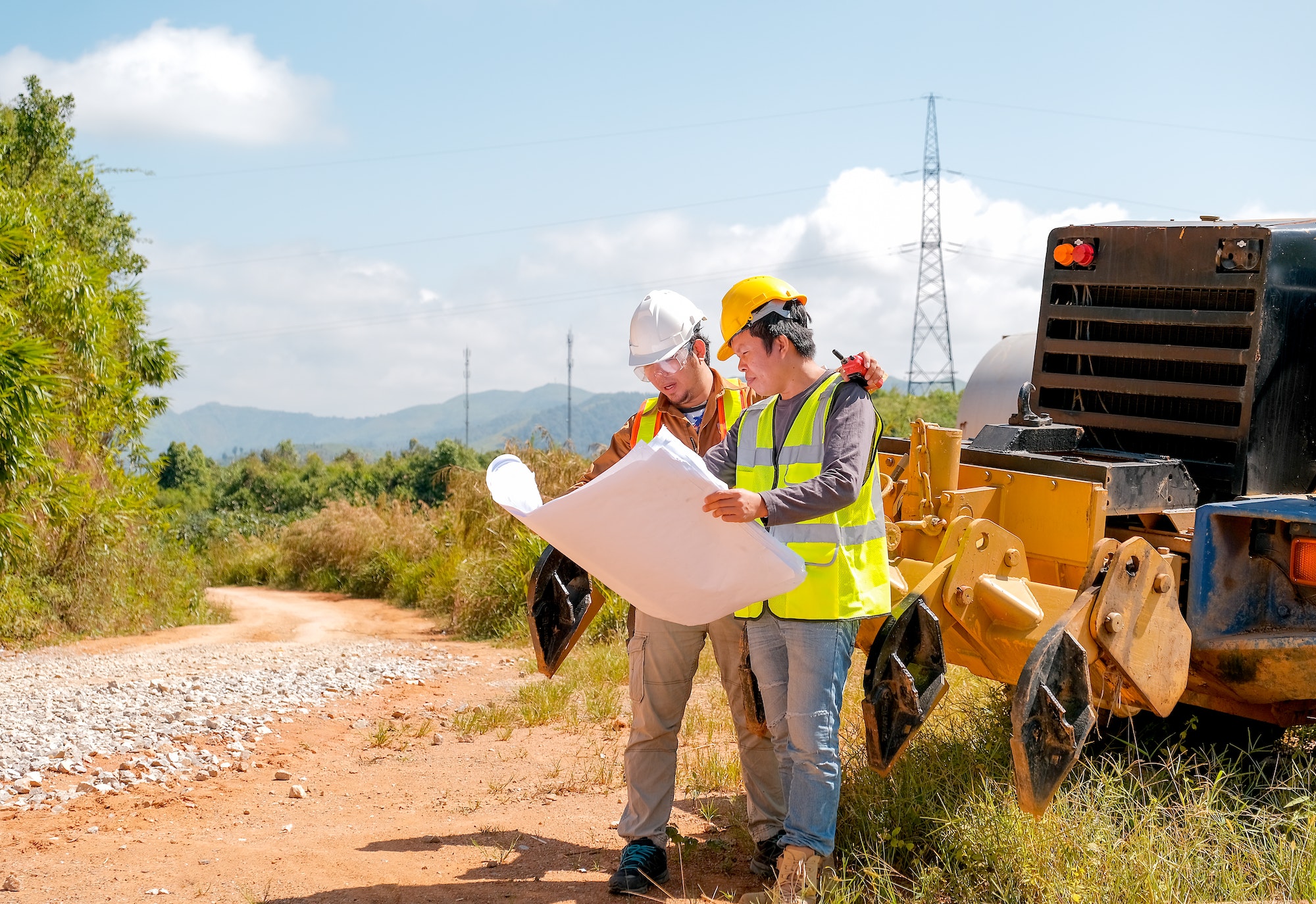 Engineer manager discuss with his team and stand in front of tractor in the area of construction.